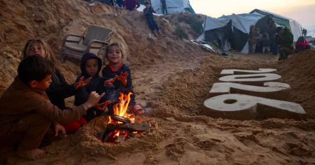 Anak-anak Palestina menghangatkan diri di dekat api unggun di samping patung pasir karya seniman Yazed Abo Jarad di Deir el-Balah di Jalur Gaza tengah [File: AFP]