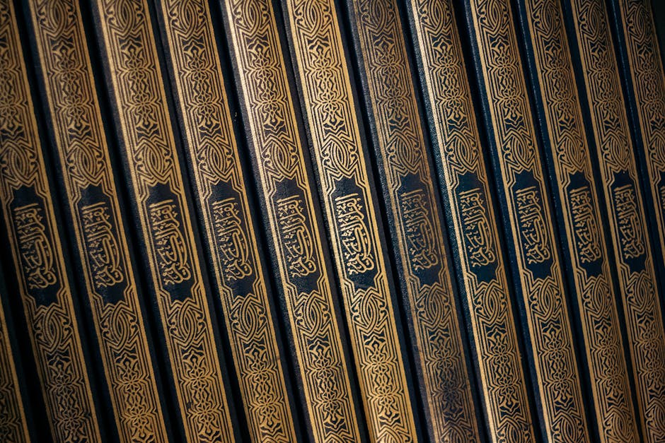 Deskripsi gambar dalam Bahasa Indonesia: Foto sebuah naskah hadis kuno dengan tulisan kaligrafi Arab yang indah di atas meja kayu tua, dikelilingi oleh tumpukan kitab-kitab klasik di sebuah perpustakaan Islam yang tenang dan penuh wibawa.