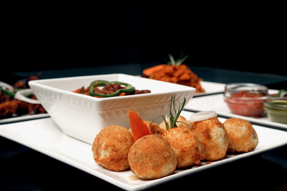 Potongan ayam goreng mentega berwarna cokelat mengkilap yang menggoda, disajikan di atas piring putih dengan taburan daun bawang dan irisan bawang bombay segar di sekelilingnya.