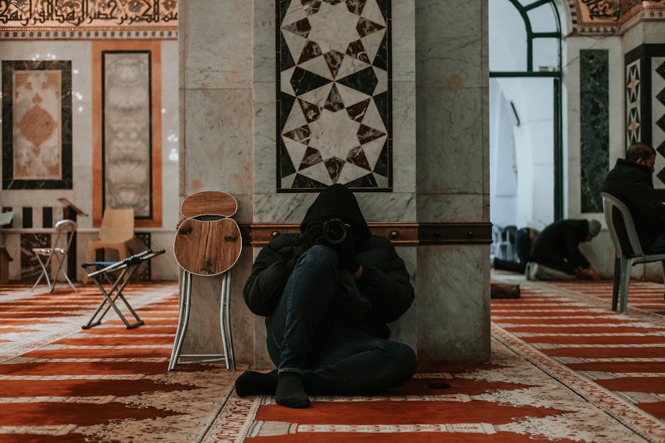 Foto sebuah mushaf Al-Quran terbuka di atas meja kayu di dalam perpustakaan klasik dengan pencahayaan hangat yang menonjolkan teks Arab yang indah dan tumpukan naskah kuno di latar belakang.